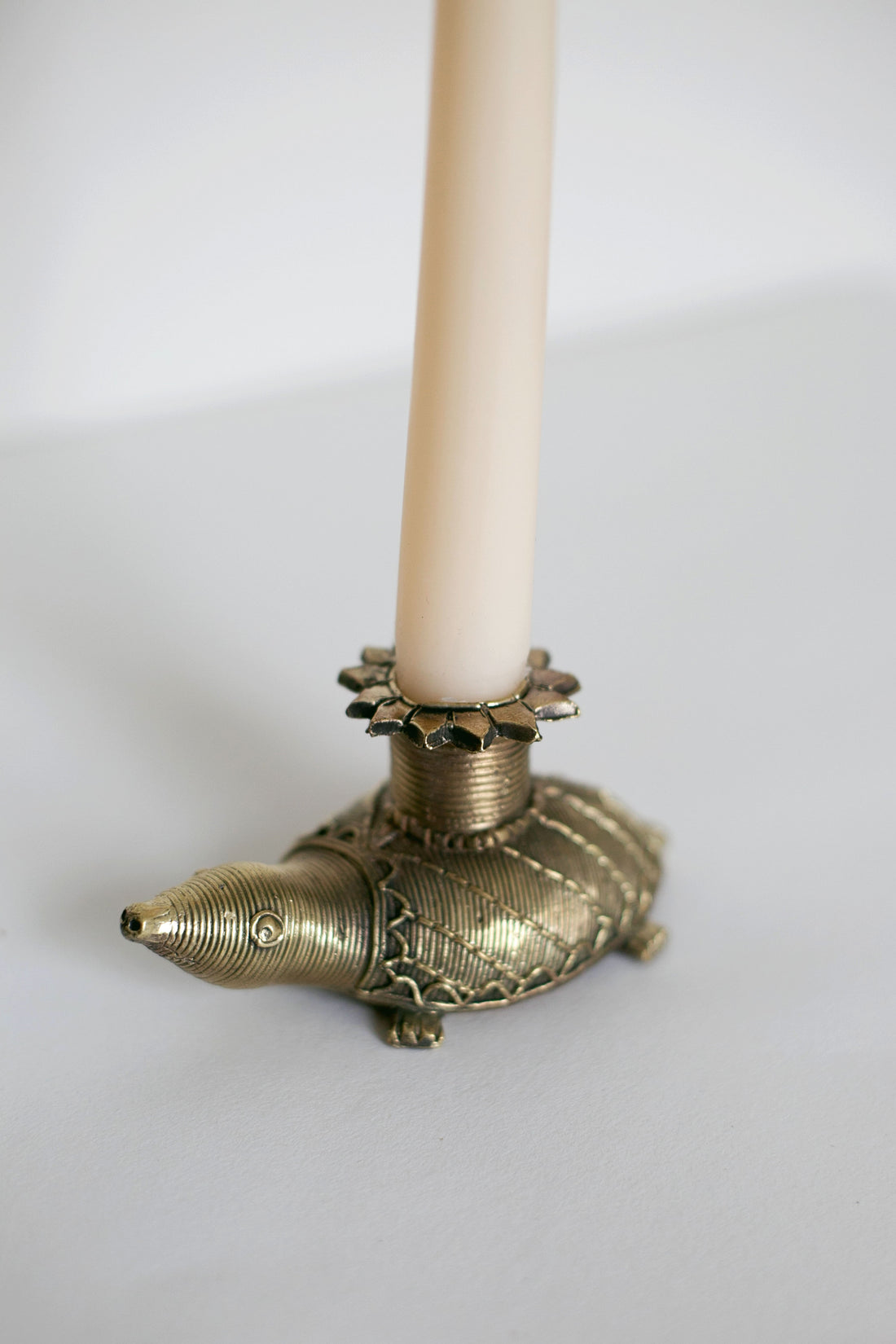 Brass turtle-shaped candle holder with engraved patterns, holding a tall cream taper candle.