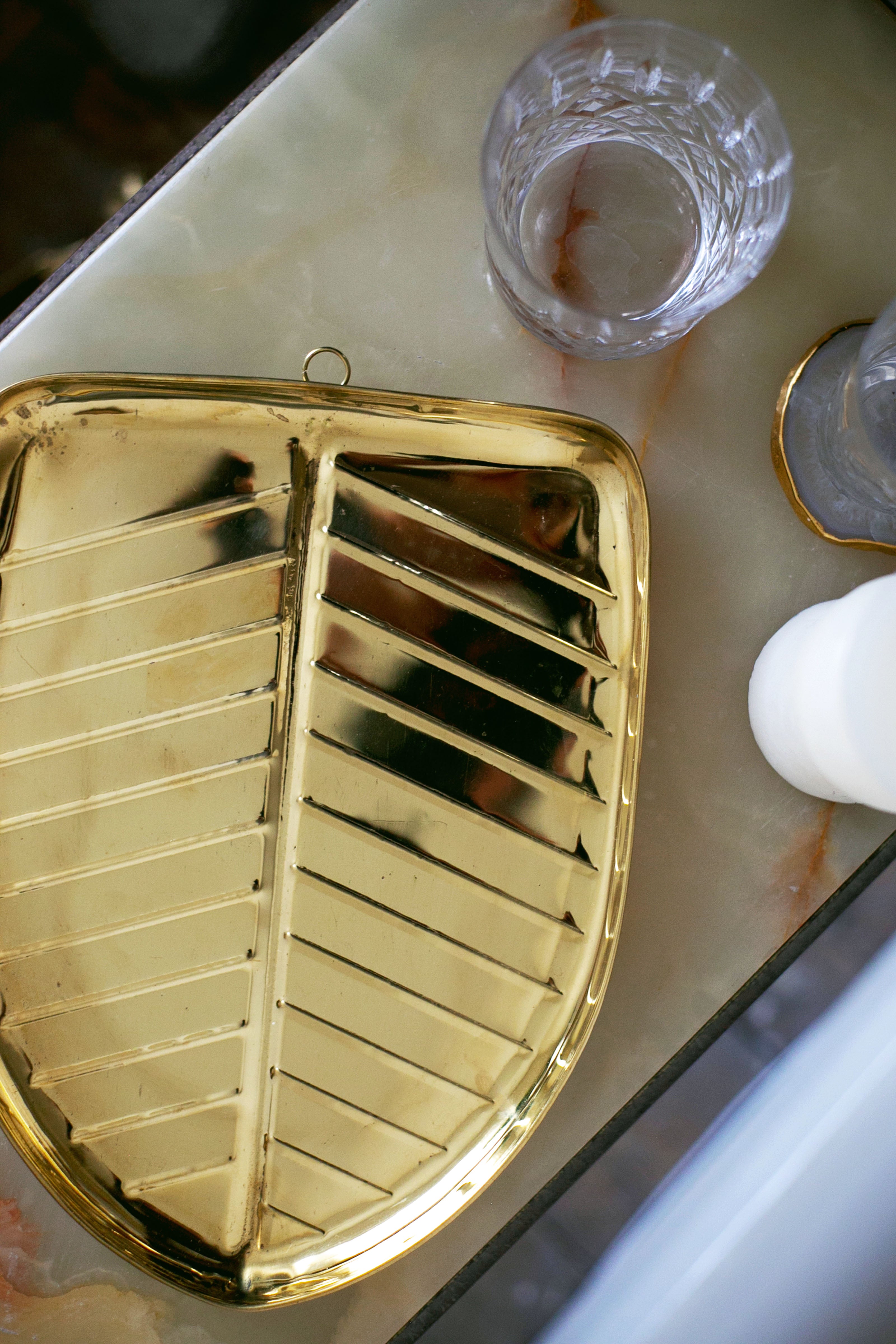 Gold leaf-shaped tray with ridged design beside a textured glass and white candle on a marble surface.