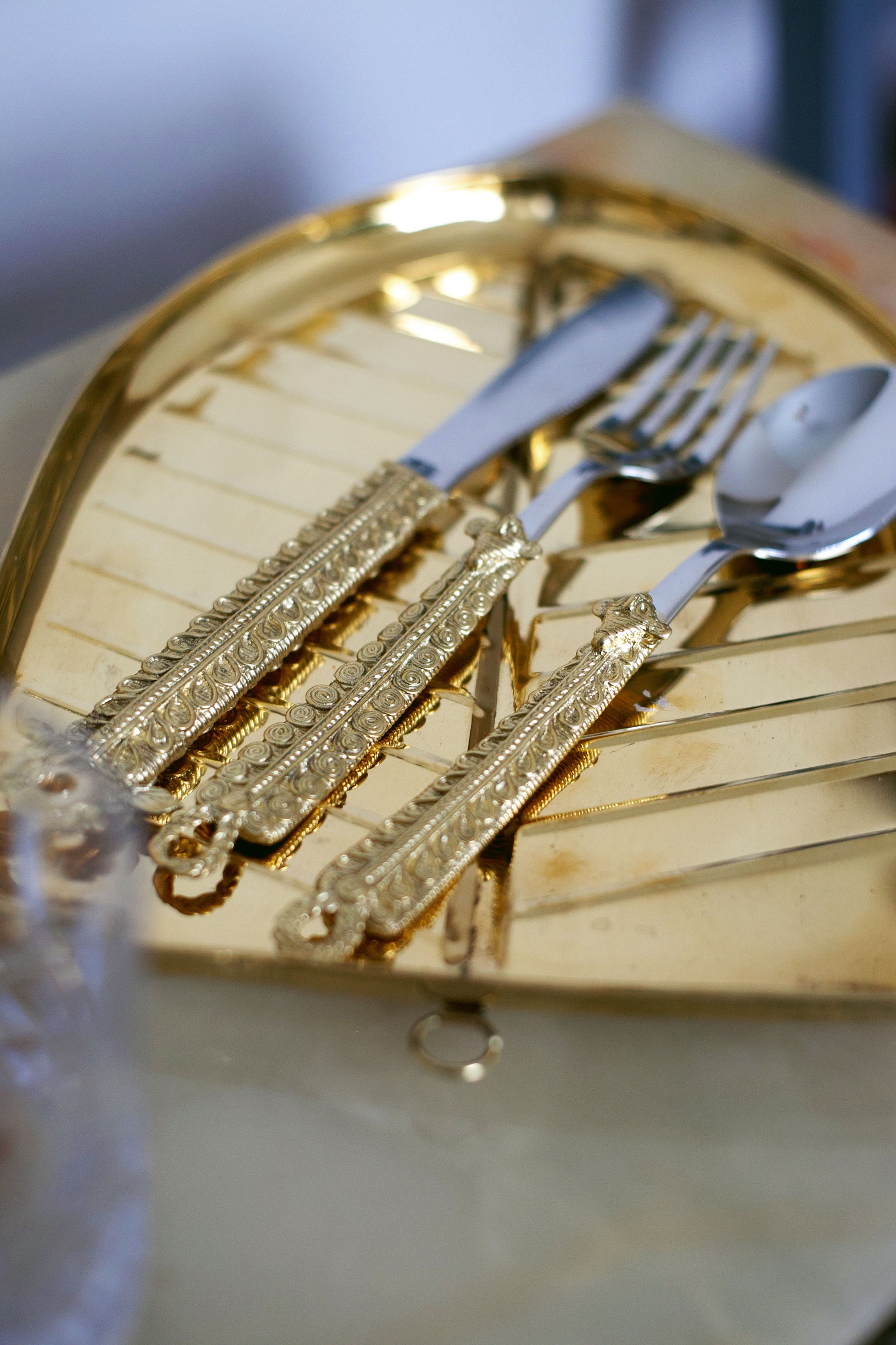 Reflective golden tray holding ornate cutlery—two forks and two spoons with intricate gold-patterned handles.