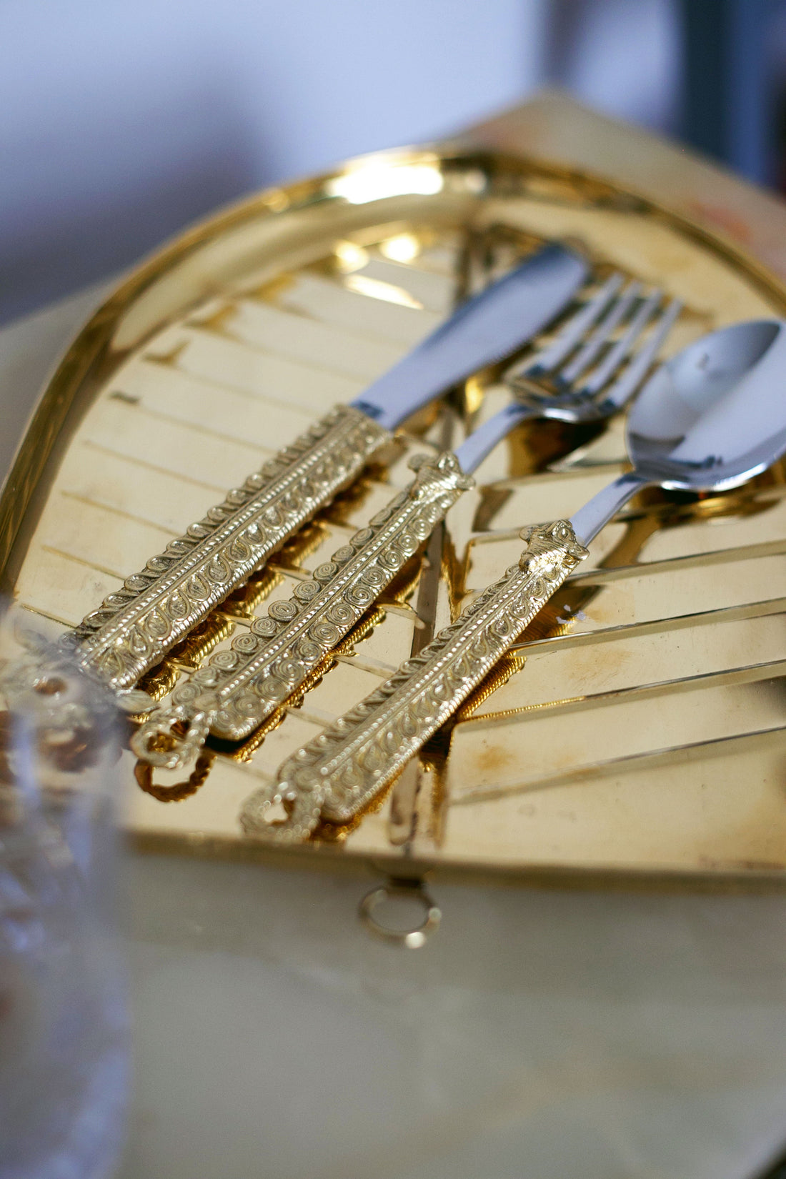 Reflective golden tray holding ornate cutlery—two forks and two spoons with intricate gold-patterned handles.