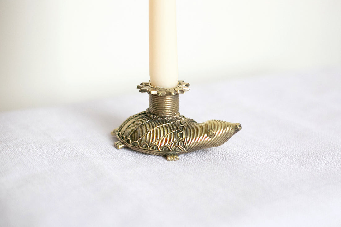 A brass candle holder in the shape of a tortoise with a gold finish, holding a white taper candle.