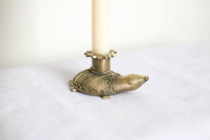 A brass candle holder in the shape of a tortoise with a gold finish, holding a white taper candle.