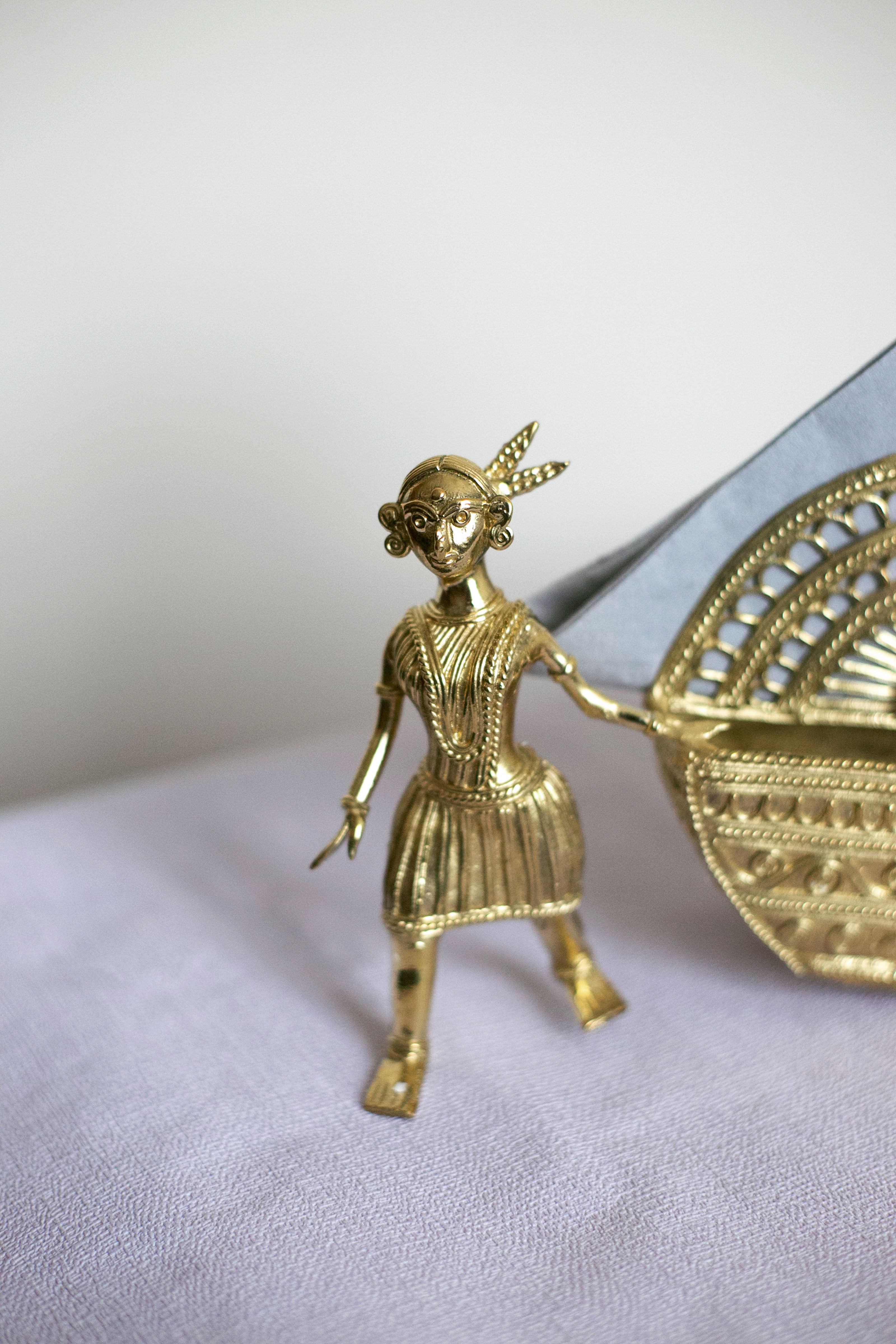 Small gold figurine of a girl holding decorative basket