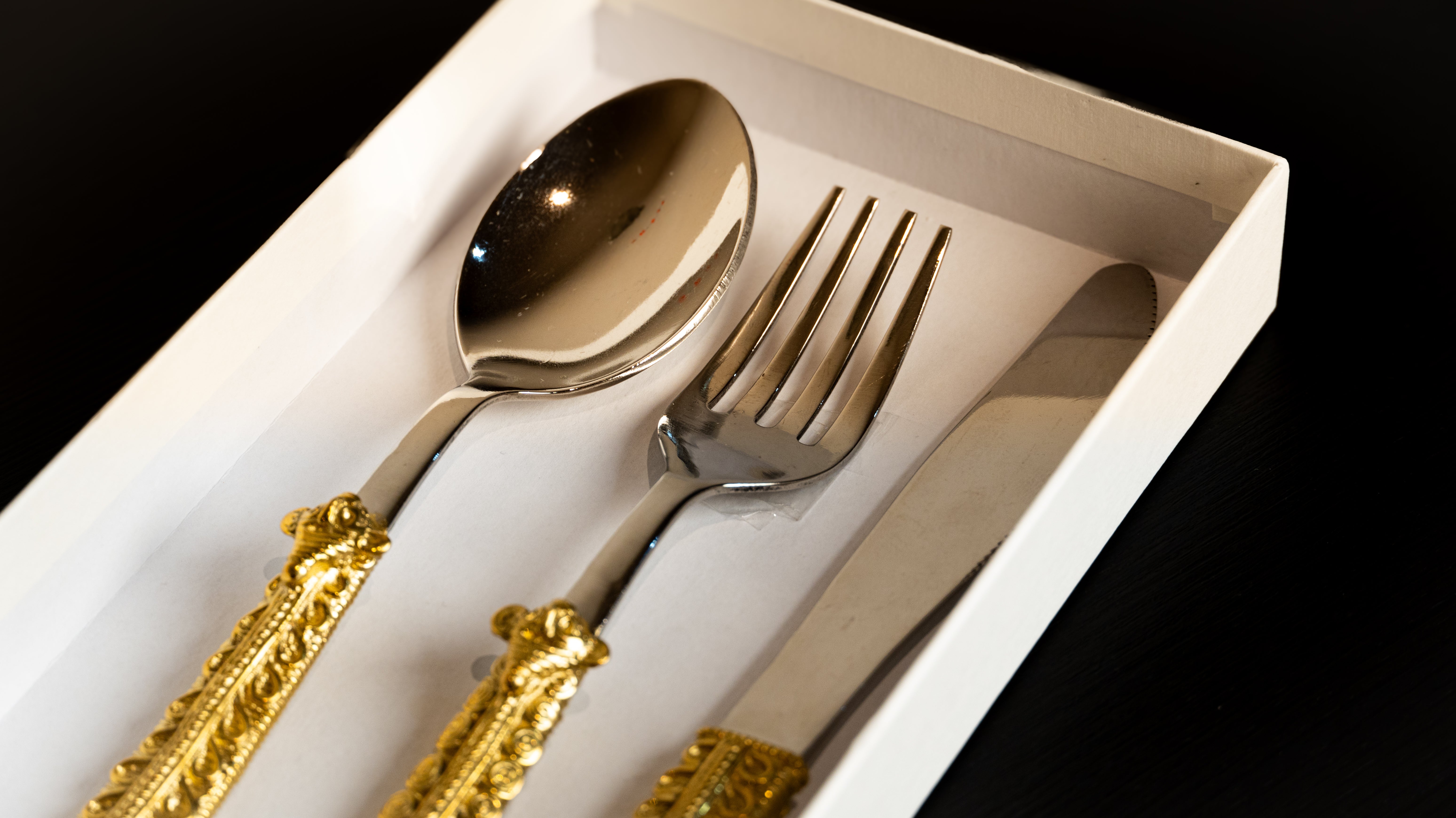 Elegant silver cutlery set with ornate gold handles in a white presentation box
