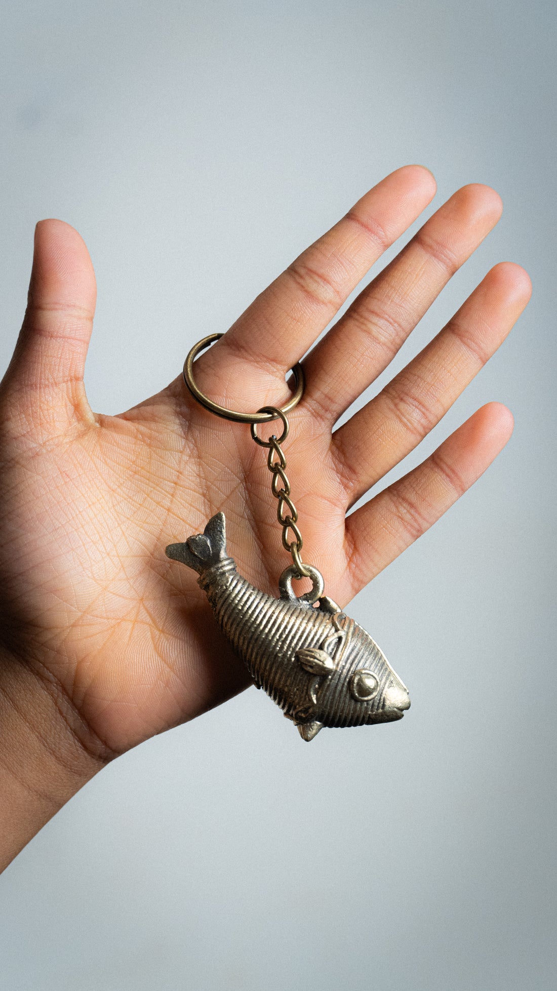 Hand holding a golden metallic fish-shaped keychain with detailed scales, fins, and eye attached to a circular ring.