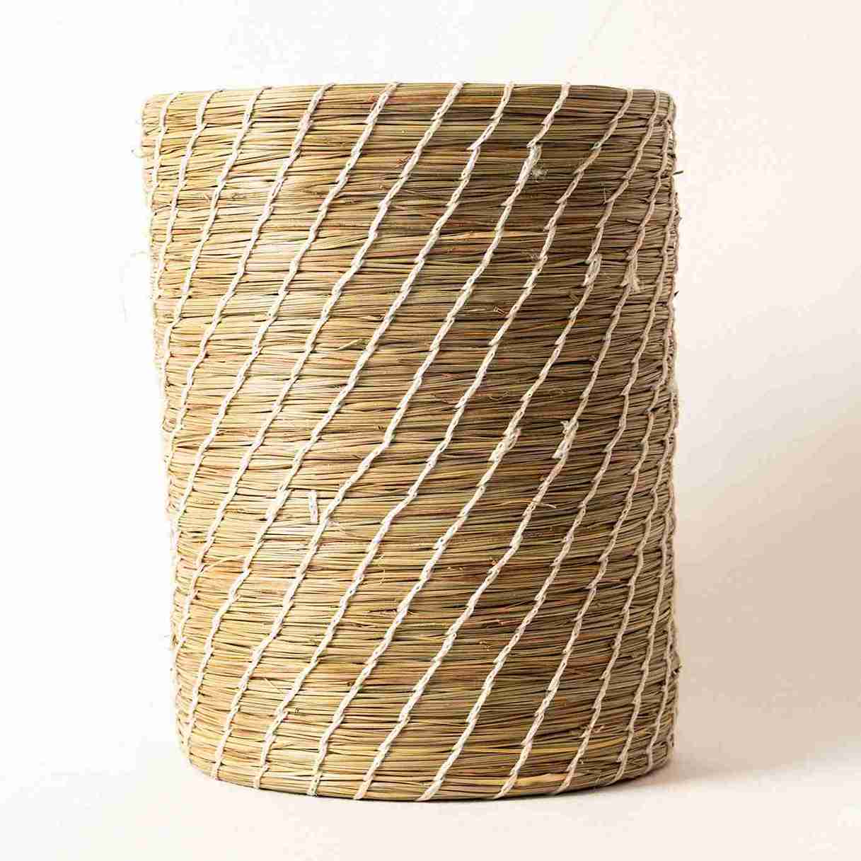 Woven cylindrical basket with natural and white stripes on a light background