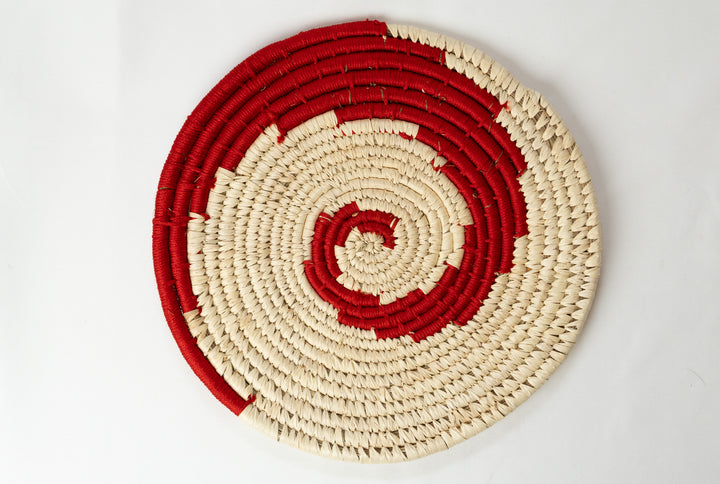 Round woven mat with concentric red and beige circles on a light gray background