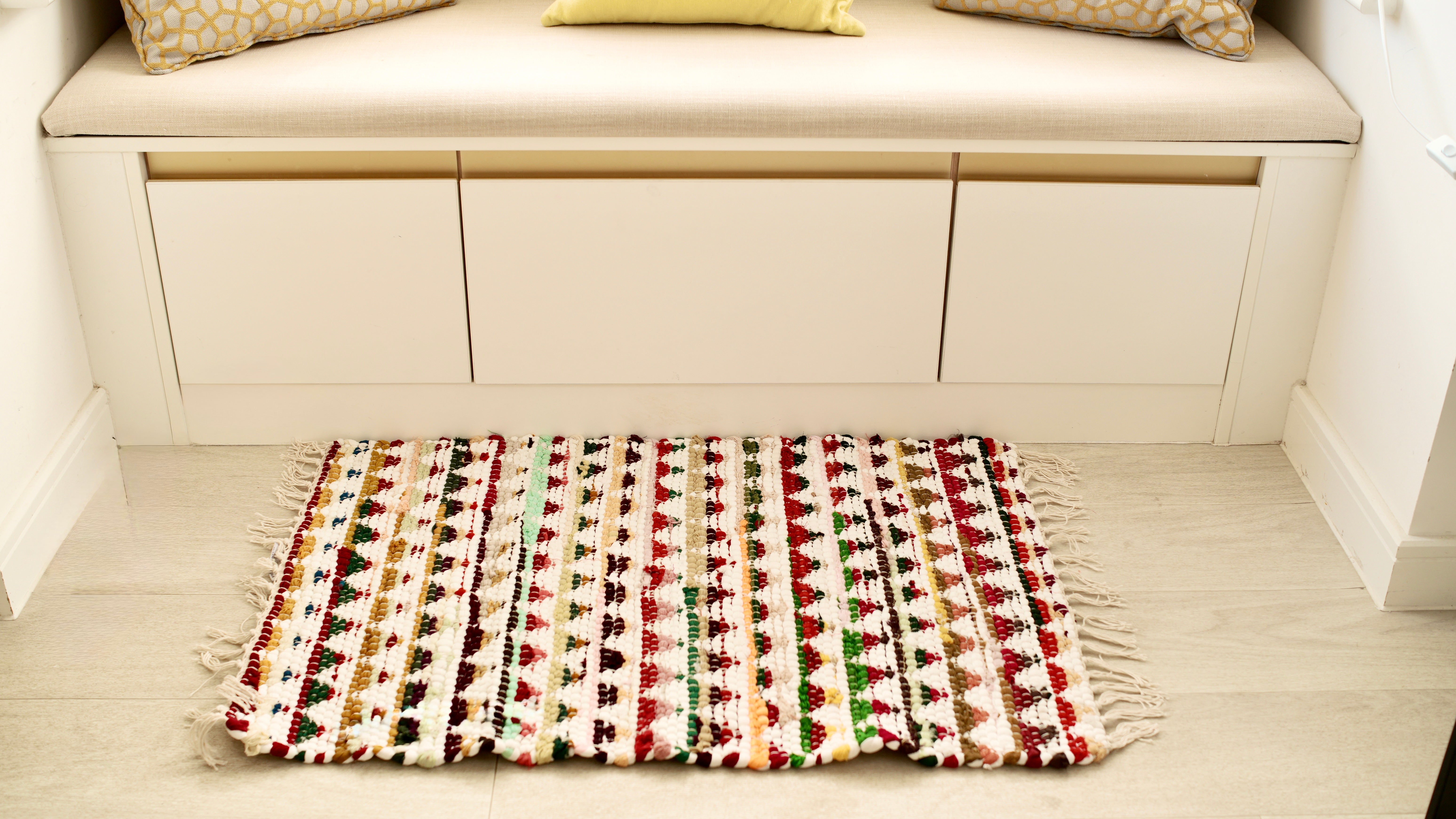 Multicolored patterned rug on a wooden floor in front of a white cabinet with cushions.