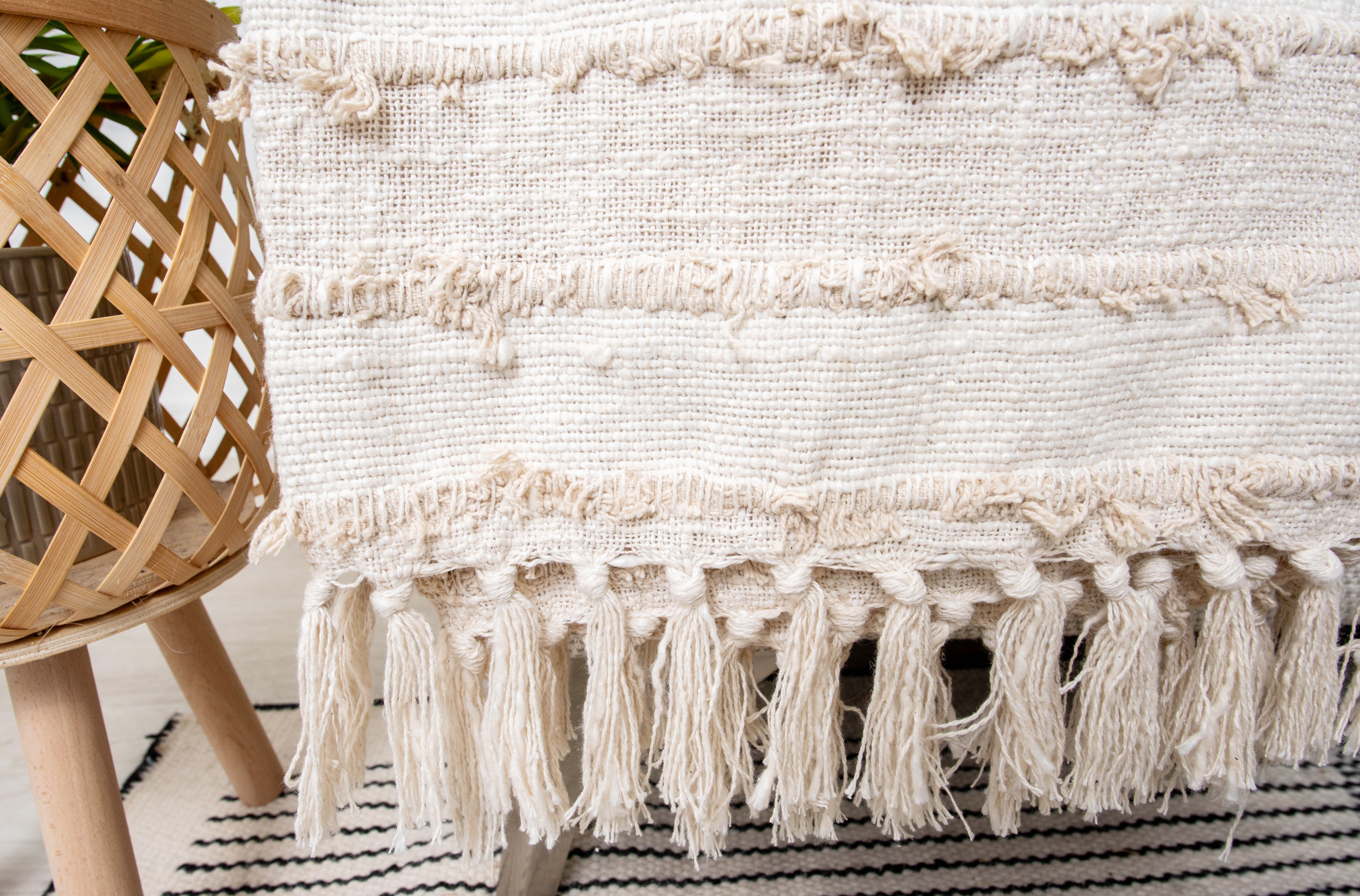 This product is a beige or ivory tufted throw blanket featuring tassels and a textured, woven design, often used for home decor on sofas or beds. 