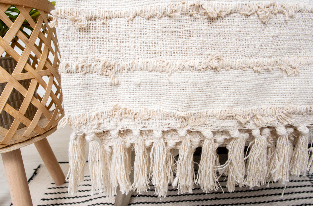 This product is a beige or ivory tufted throw blanket featuring tassels and a textured, woven design, often used for home decor on sofas or beds. 