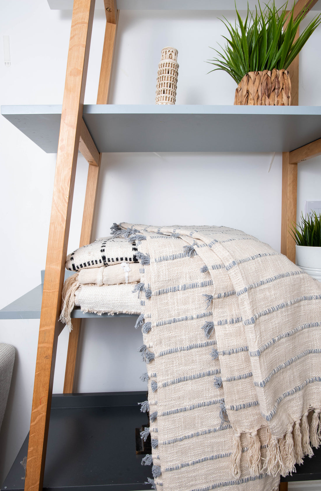 Folded striped blankets on shelf with plants.