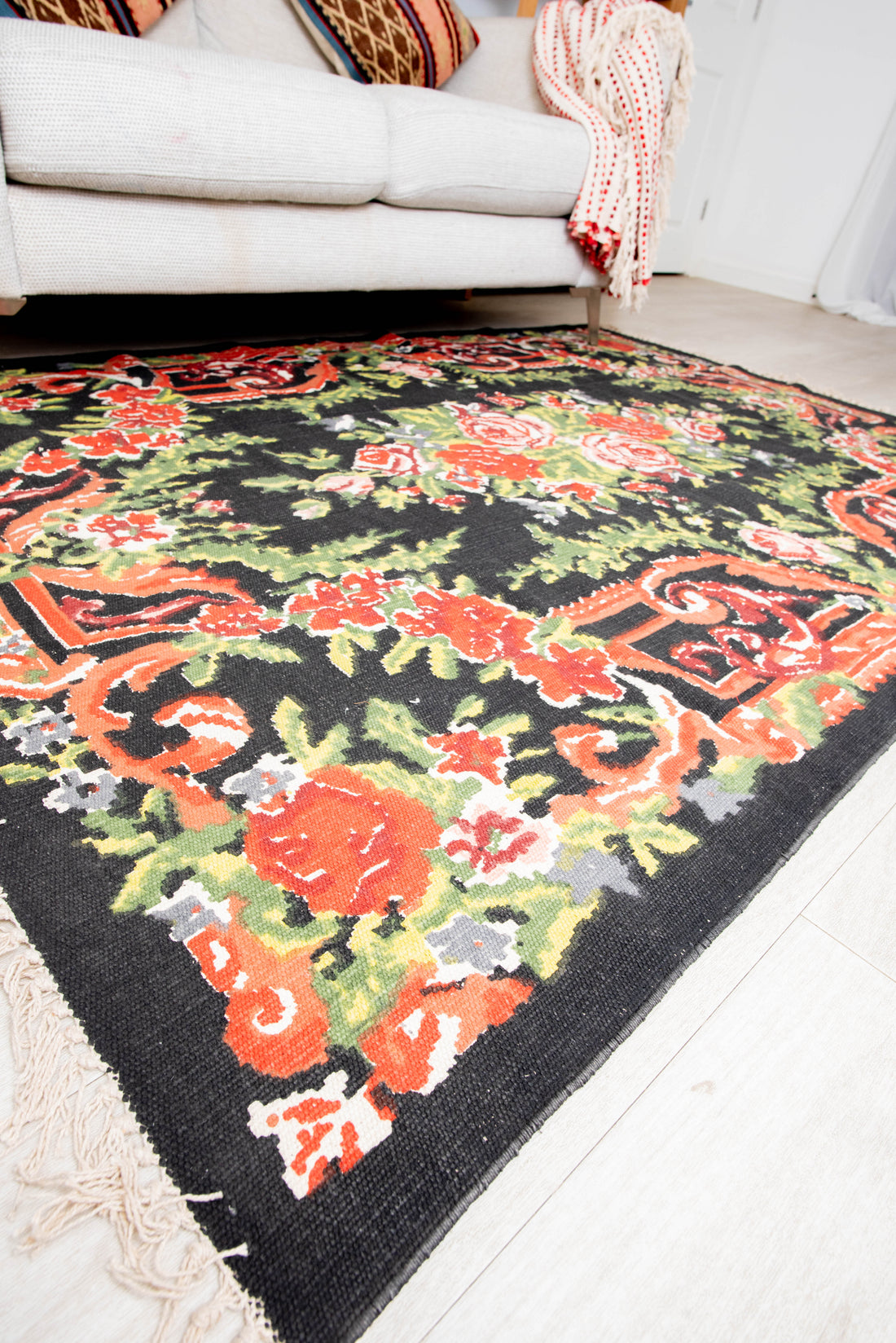 A rectangular, floral design cotton rug in shades of black, red, and green, placed on a floor with a white door in the background.