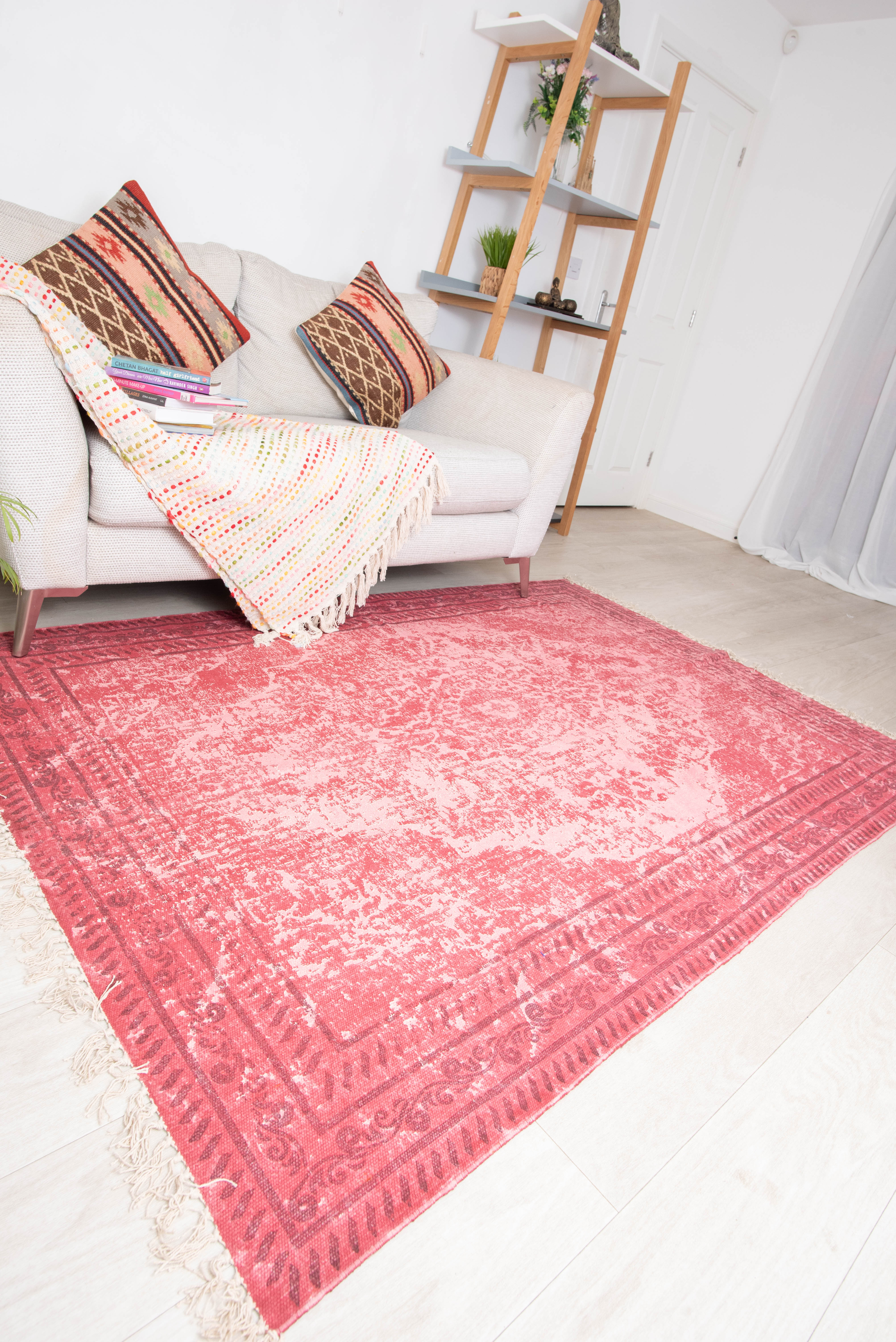 A traditional red cotton rug with an intricate geometric pattern, placed on a floor in a living space.