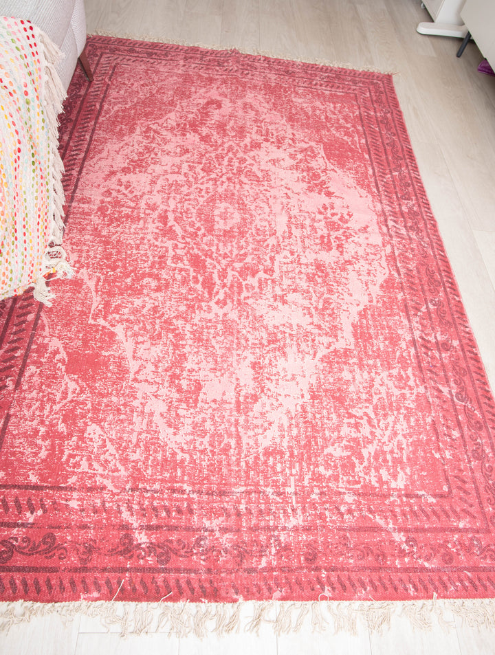 A traditional red cotton rug with an intricate geometric pattern, placed on a floor in a living space.