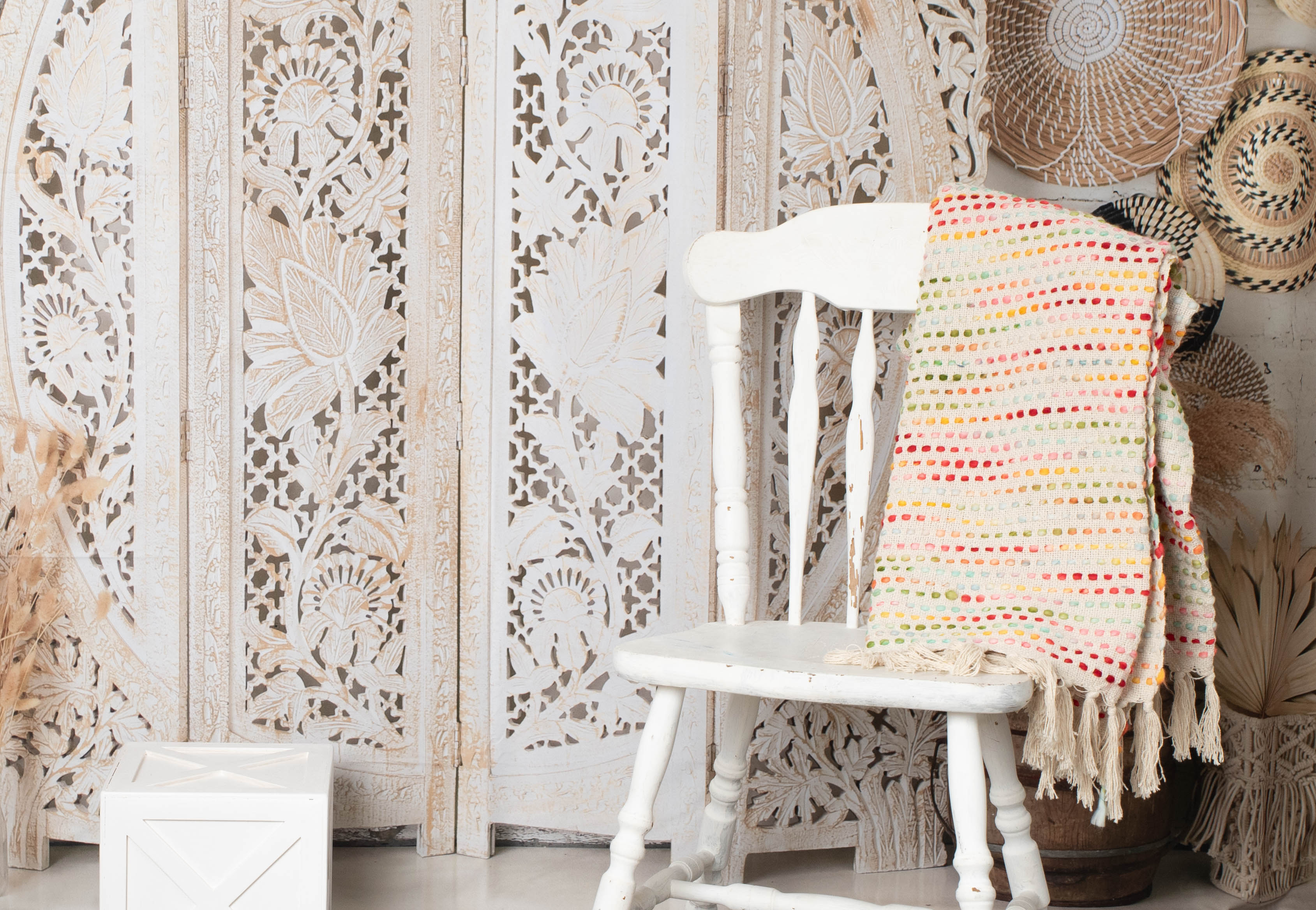 Multicolor woven throw blanket with fringe draped over white chair