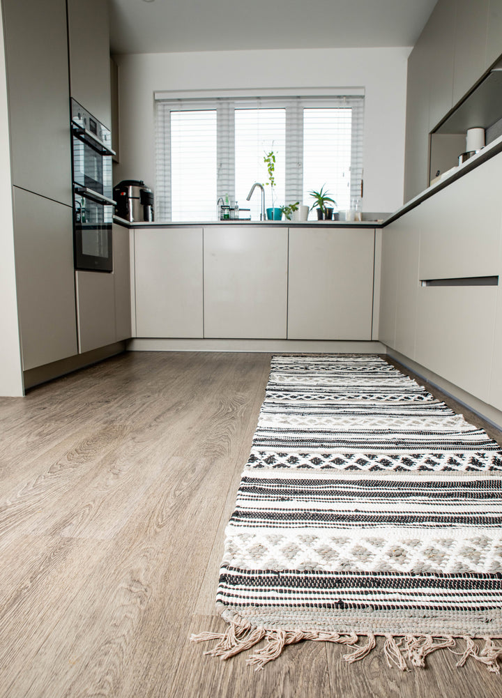 A striped runner rug with a geometric pattern placed on a wooden floor in a kitchen setting, leading to a doorway.