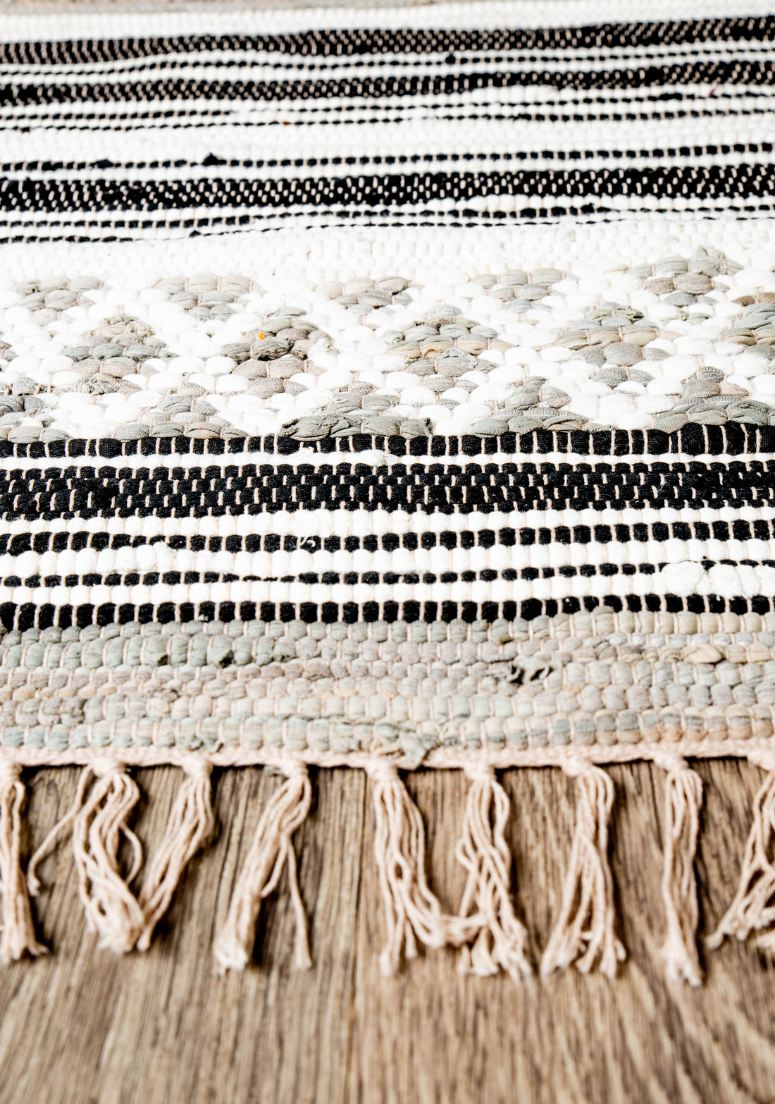 Traditional handwoven textile in gray and neutral shades with geometric motifs and fringed edge