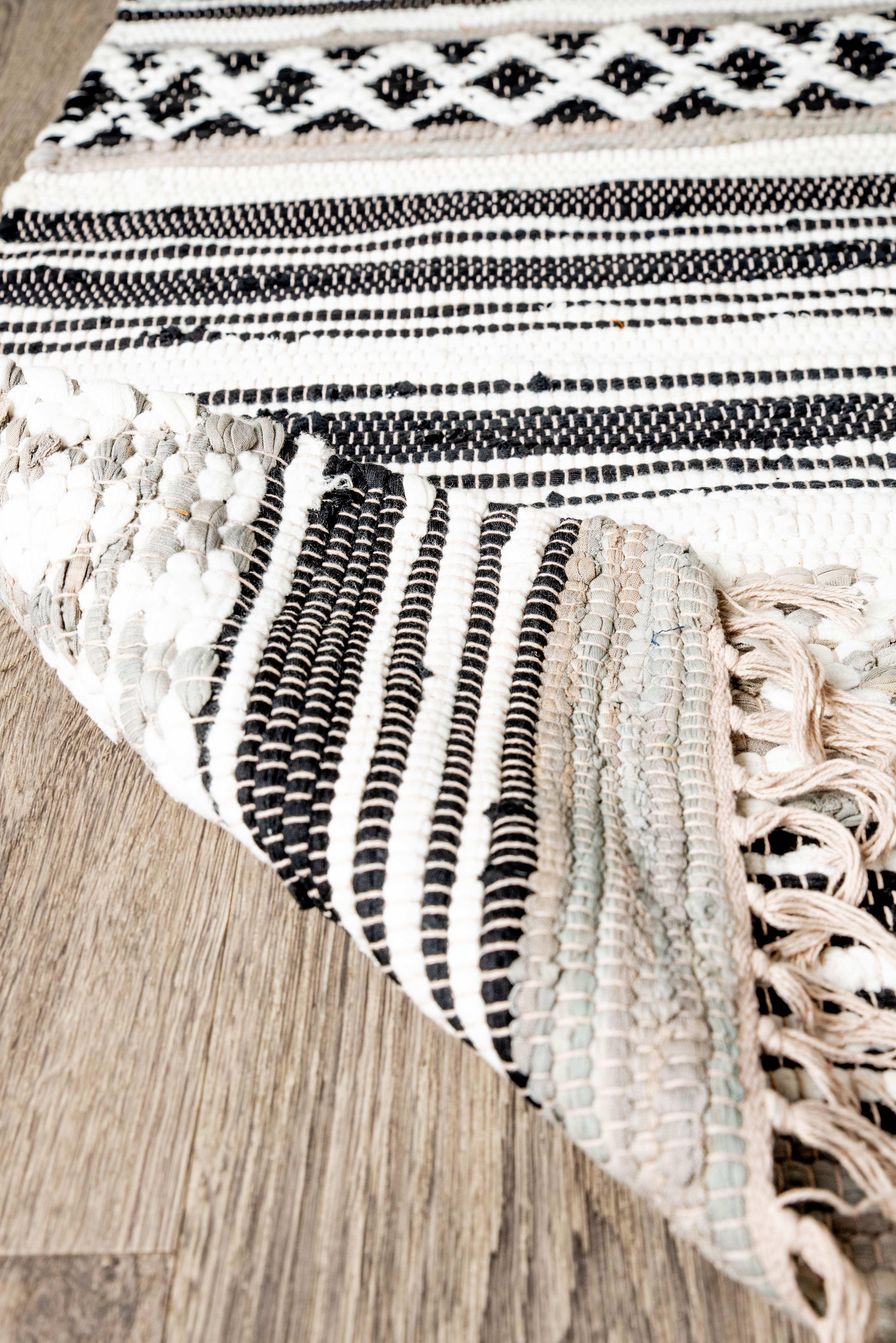 Handwoven rug with black and white geometric stripes and diamond motifs on wooden floor