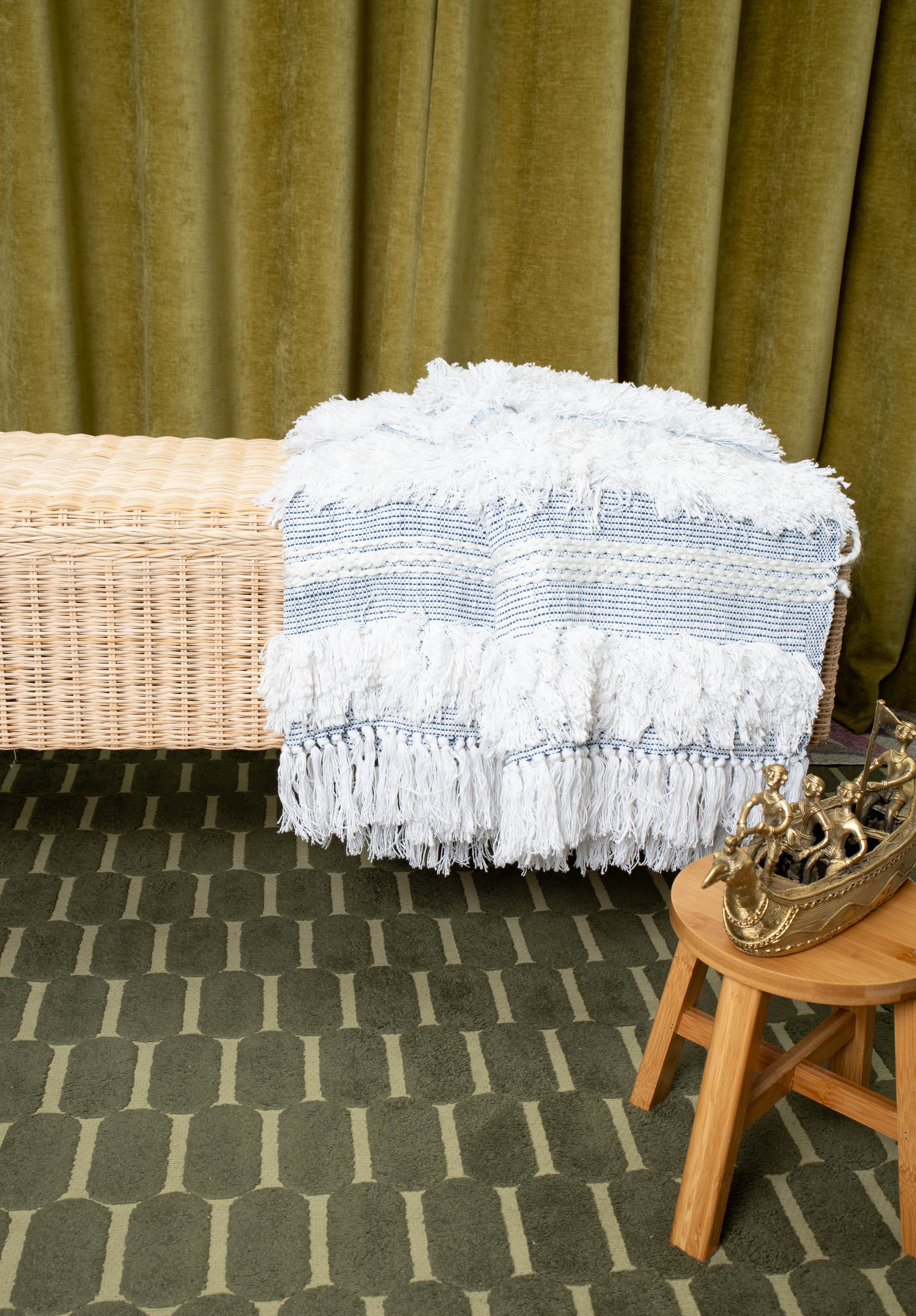 Woven bench with fringed white and blue blanket styled in cozy interior