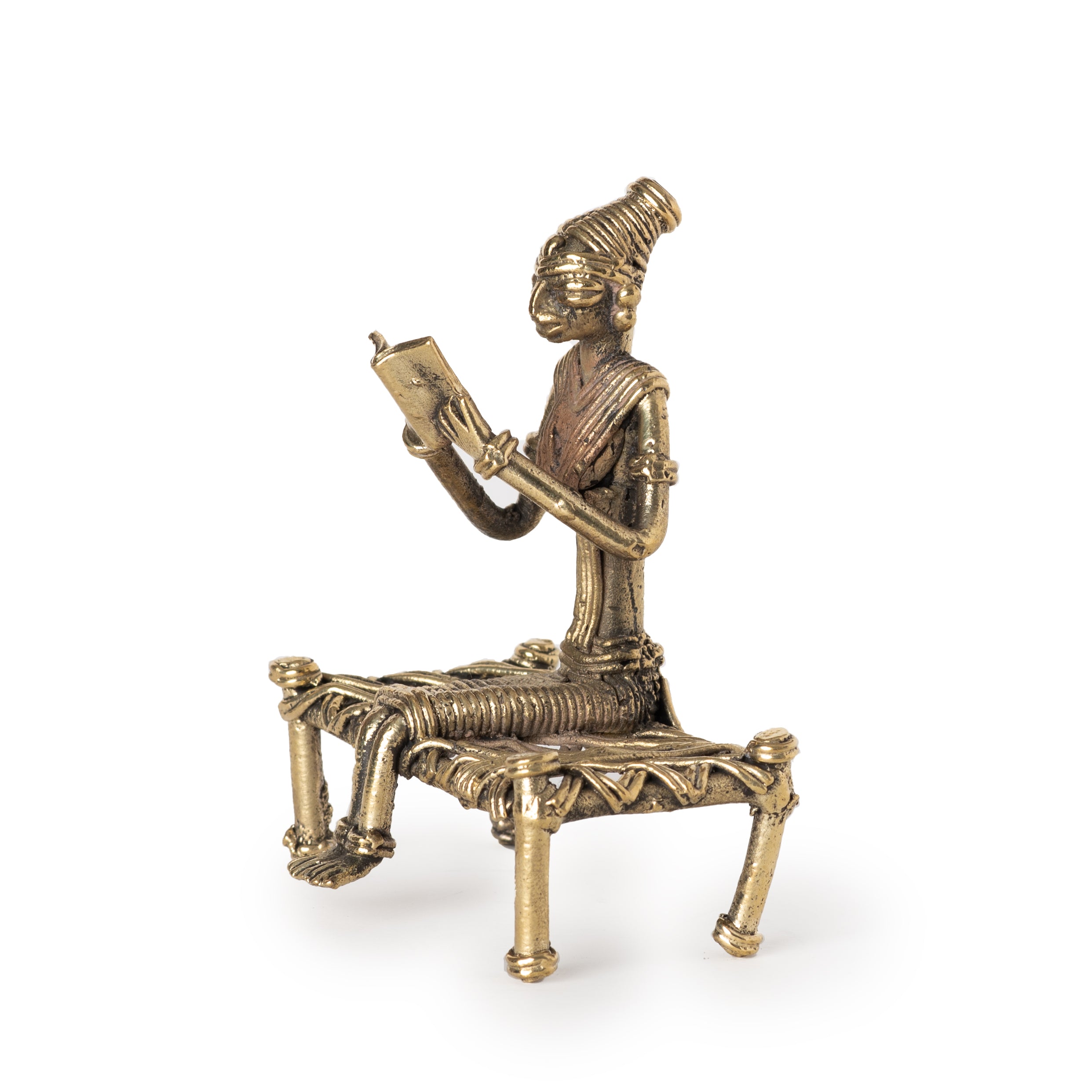 This vintage-style handmade brass figurine is a "Tribal Lady Reading Book on Cot" showpiece created using the ancient Indian Dhokra lost-wax casting technique. 