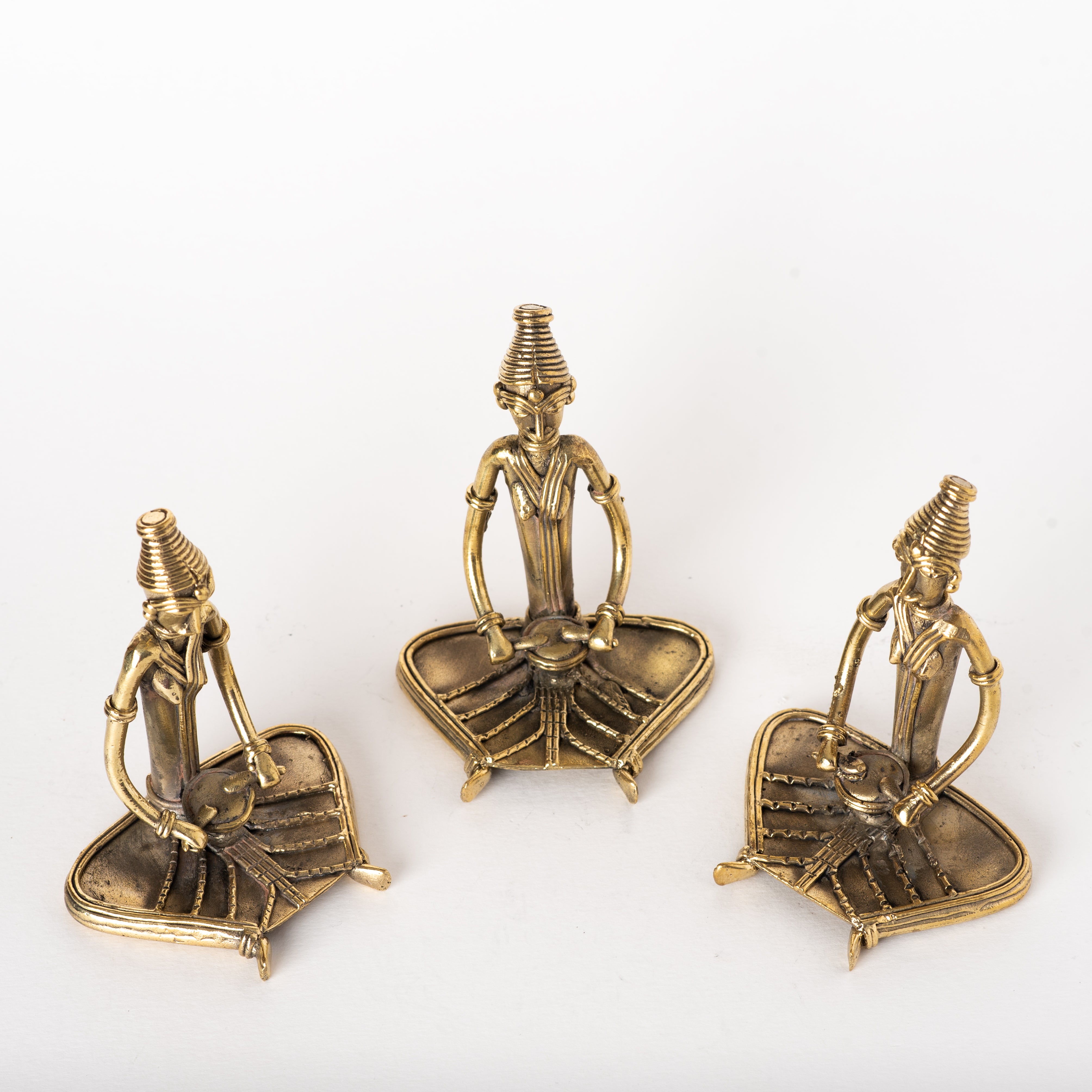 Three brass metal sculptures of sitting women musicians on a round black table, with a green plant in the background.