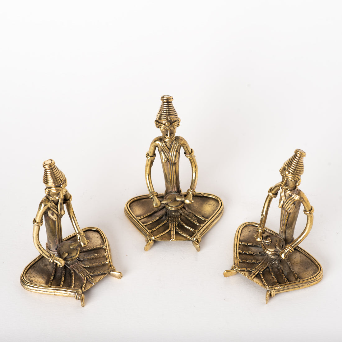 Three brass metal sculptures of sitting women musicians on a round black table, with a green plant in the background.