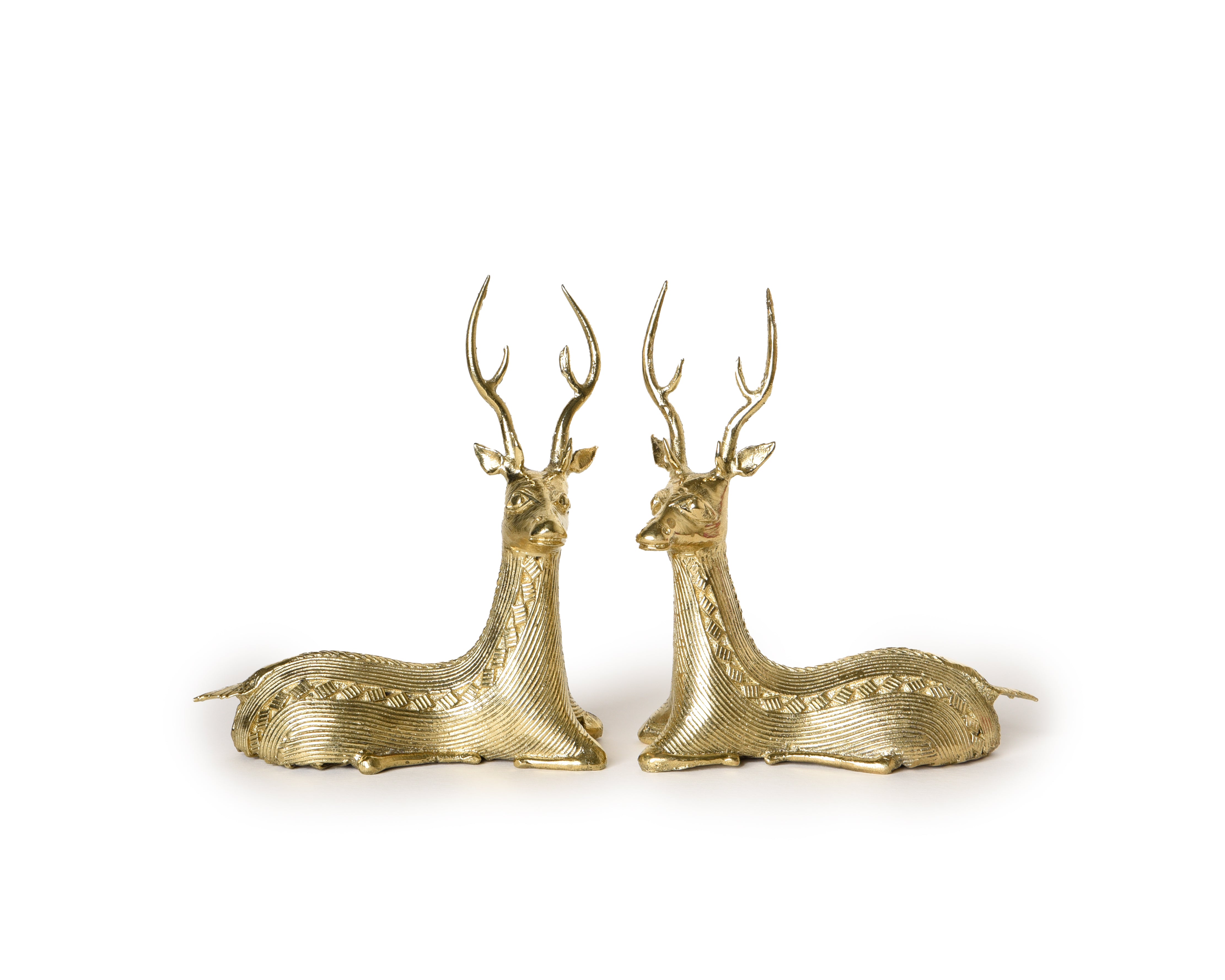 A pair of handmade brass sitting deer sculptures with detailed depiction of the deer's muscular form and serene expressions.
