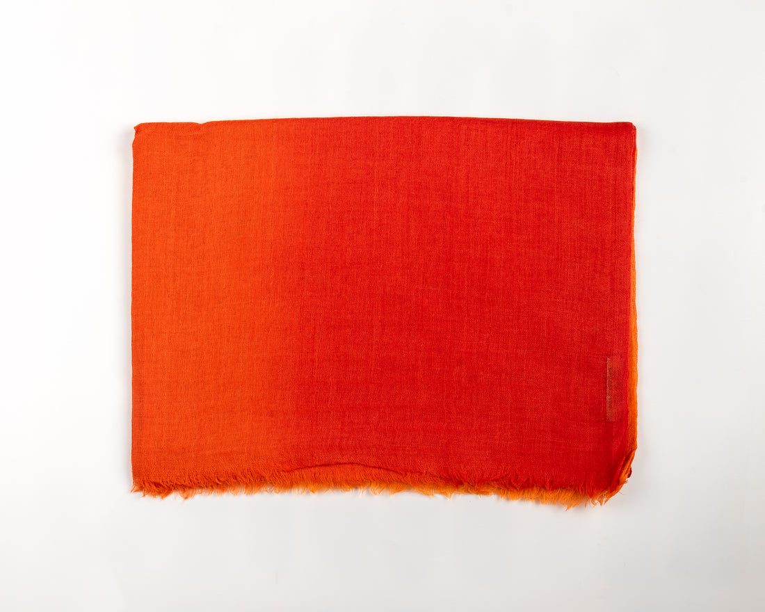 Close-up of a textured fabric with a gradient color pattern, transitioning from bright orange at the bottom to deep red at the top, with frayed edges along the lower edge.