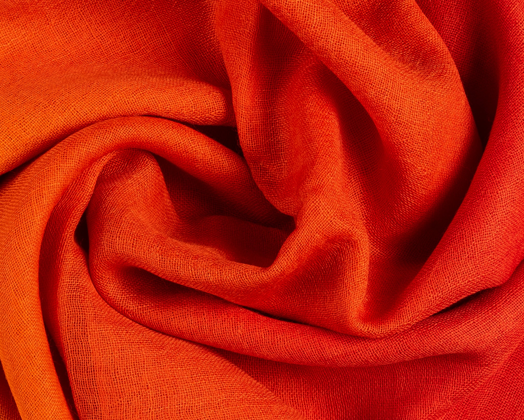Close-up of vibrant orange linen fabric with a visible fine weave, draped in soft, swirling folds.