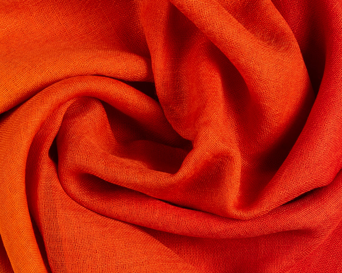 Close-up of vibrant orange linen fabric with a visible fine weave, draped in soft, swirling folds.