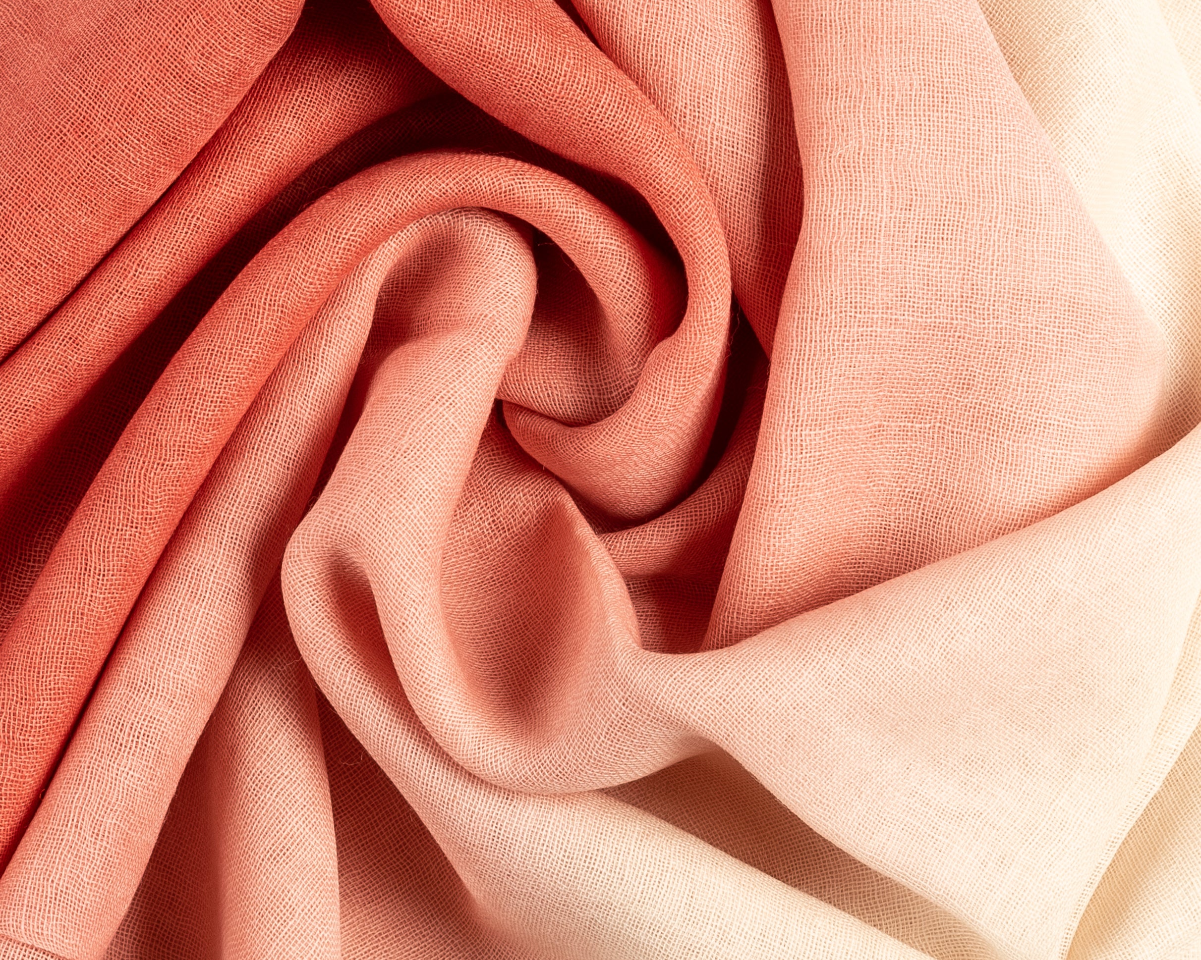 Close-up of cream to coral pink gradient fabric with soft folds and textured weave
