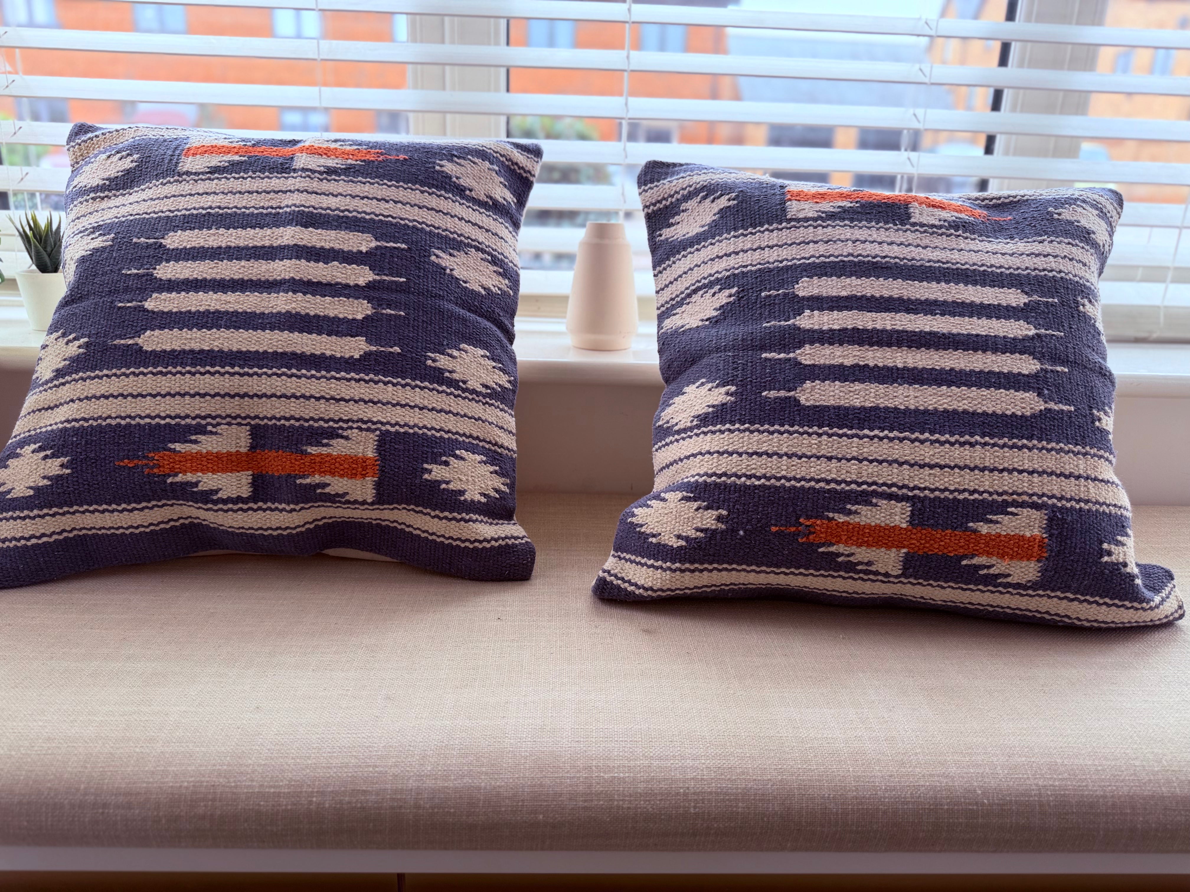 Two patterned pillows on a window sill with blinds in the background