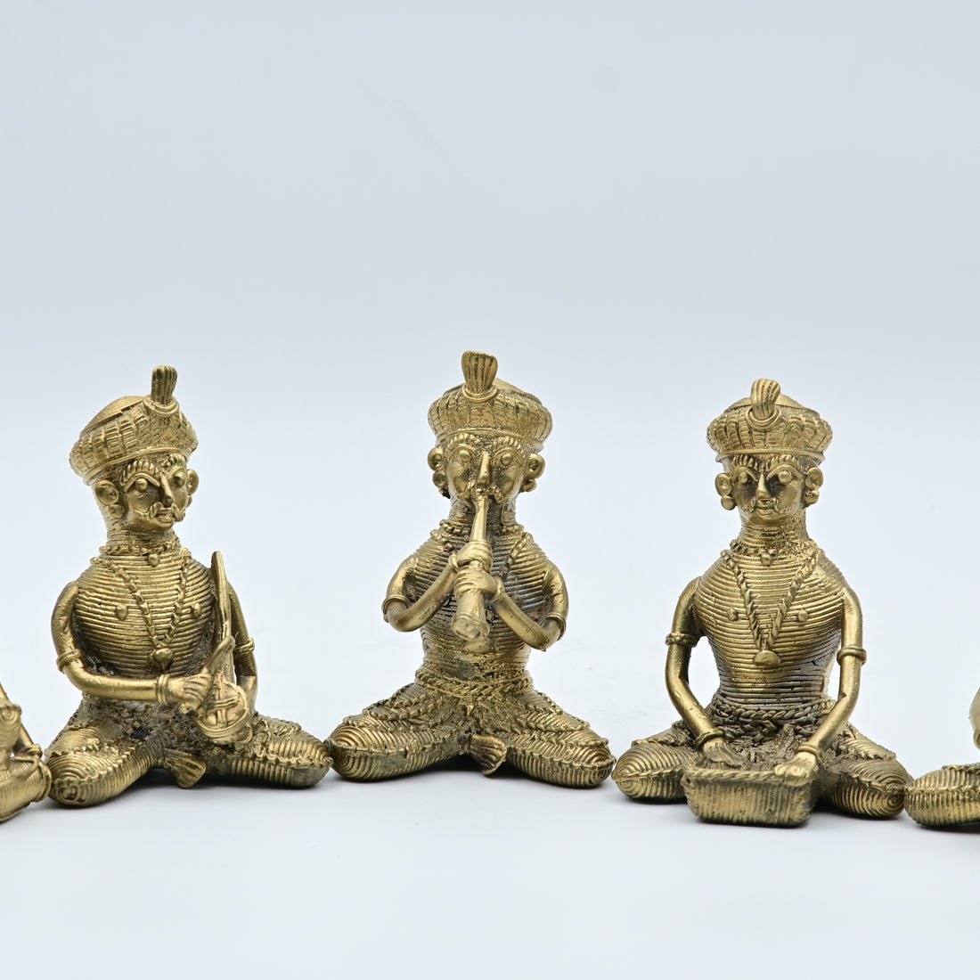 A set of five gold-colored statues of tribal musicians playing musical instruments, sitting in a row.