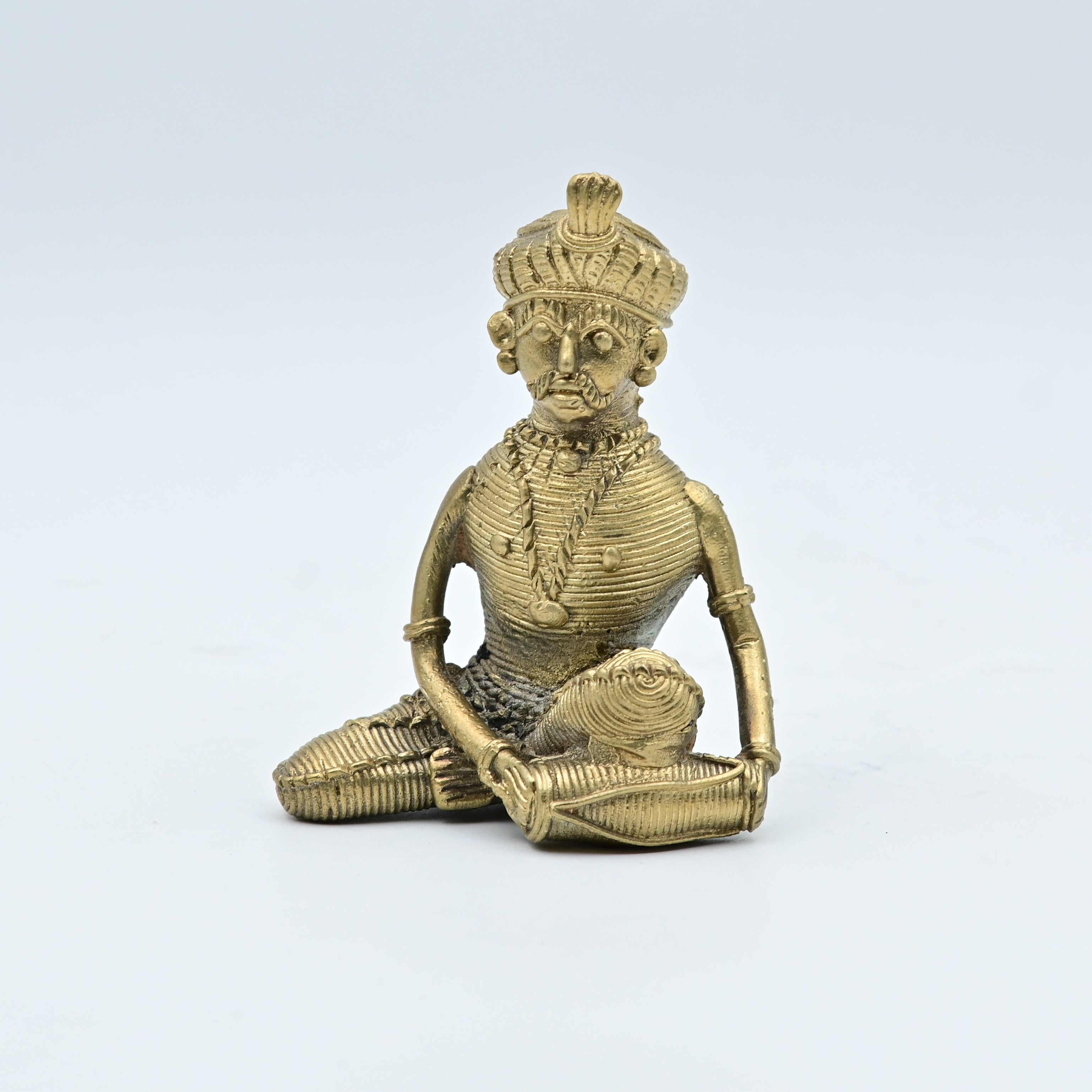 This item is a Dhokra art brass statue depicting a tribal musician playing a drum. 