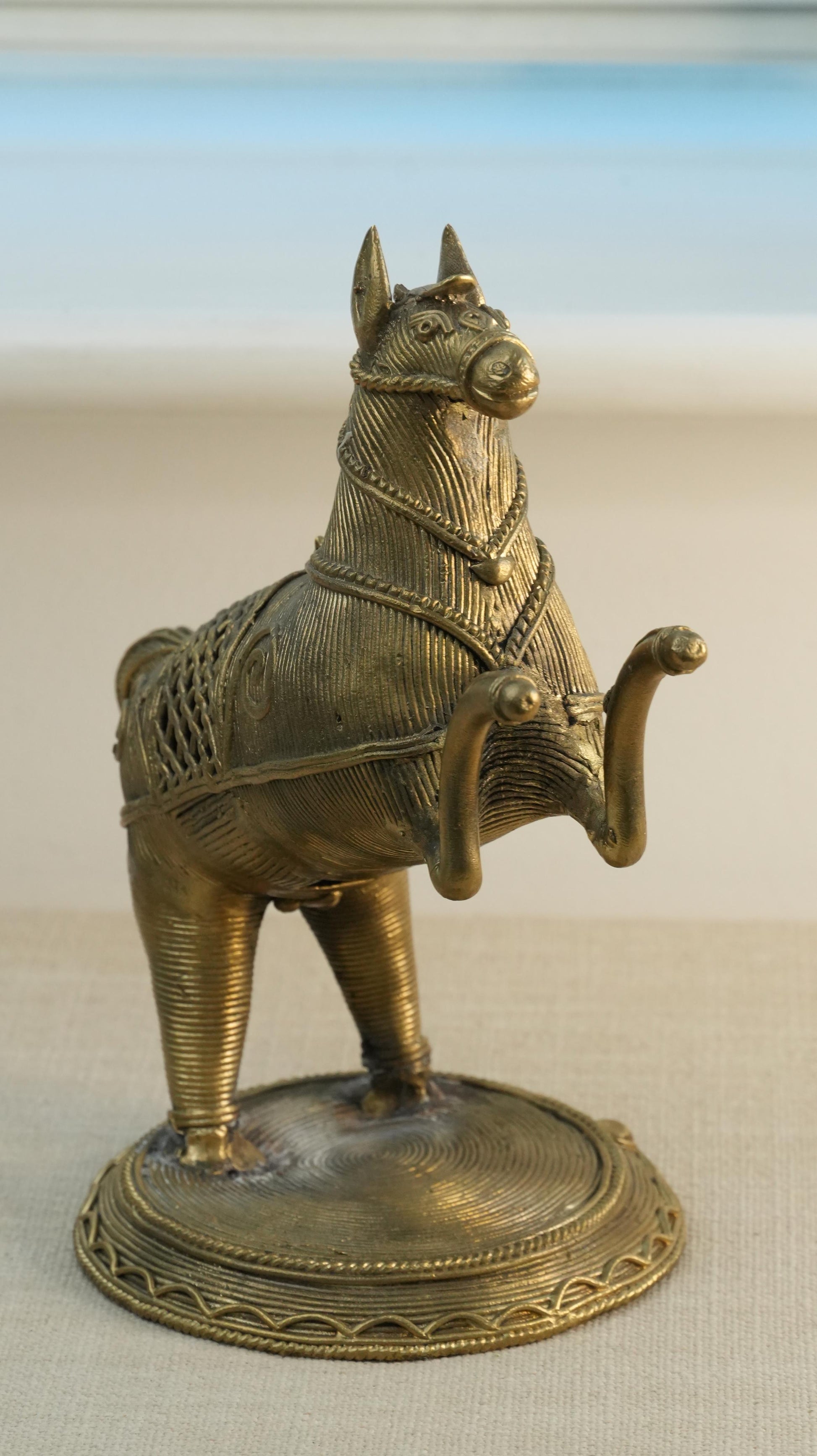 Bronze horse statue on a beige surface with a light blue gradient background