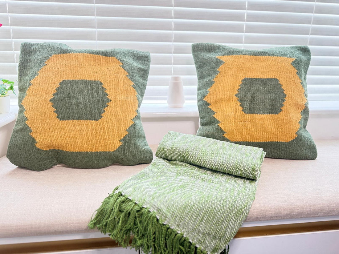 Two green pillows with orange geometric patterns and a matching green blanket on a couch.