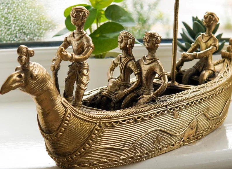 A bronze-colored metal statue depicting a ship with figures riding on it, placed on a windowsill.