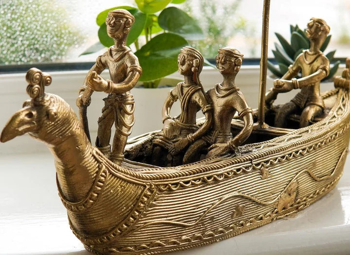 A bronze-colored metal statue depicting a ship with figures riding on it, placed on a windowsill.