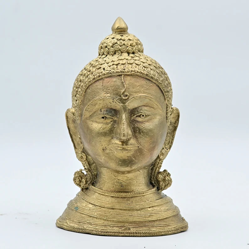 A brass statue of the Buddha with a serene expression, featuring intricate carvings and a metallic finish.