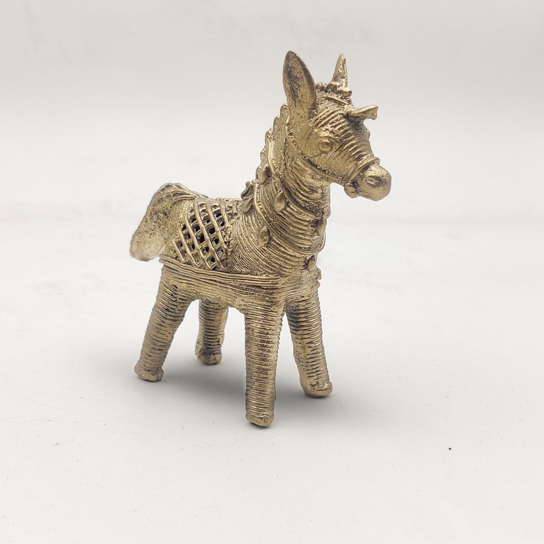 A gold-colored Dhokra horse figurine statue placed on a surface.