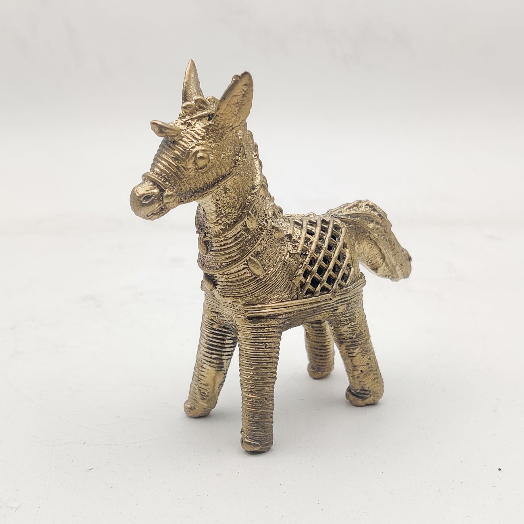 A gold-colored Dhokra horse figurine statue placed on a surface.