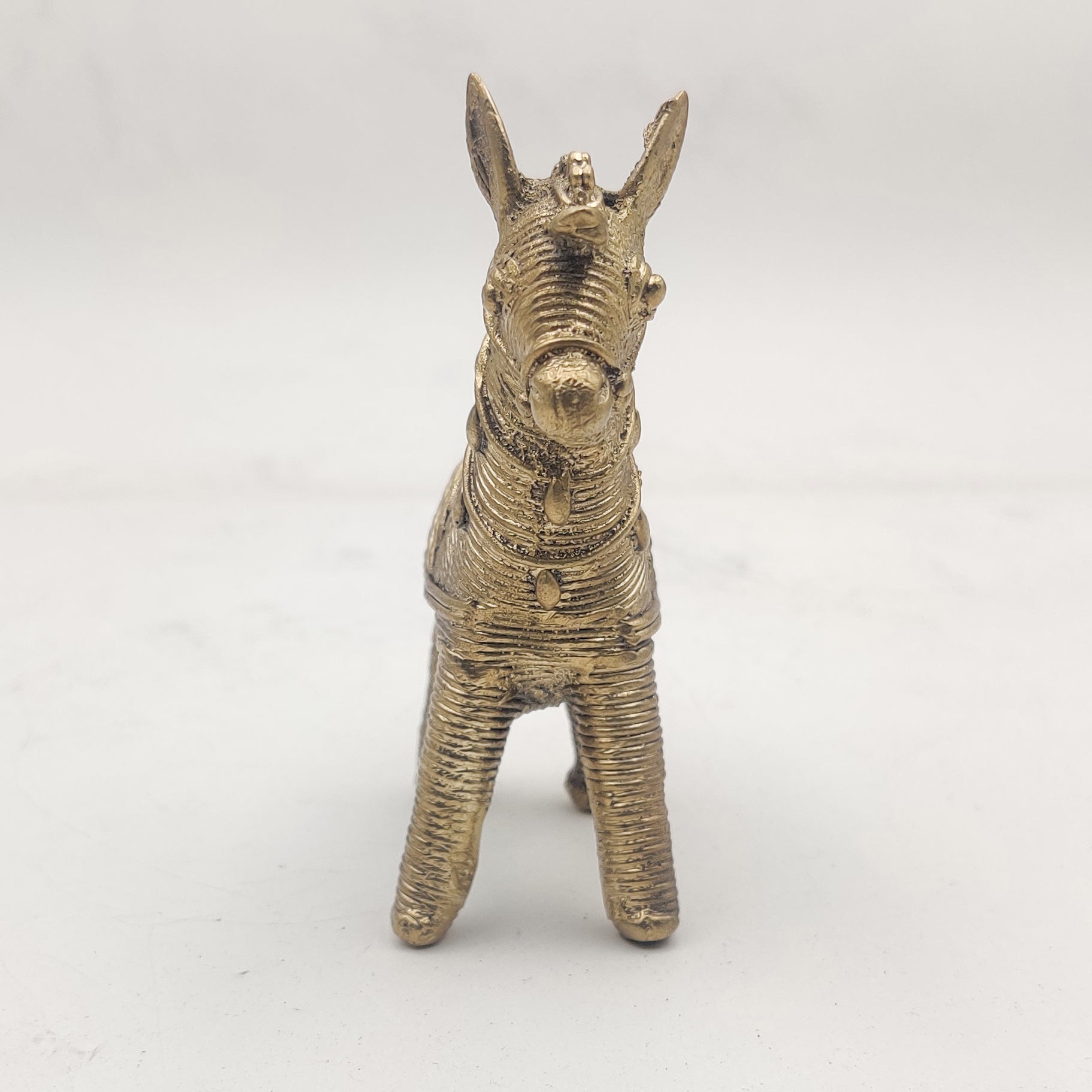 A gold-colored Dhokra horse figurine statue placed on a surface.