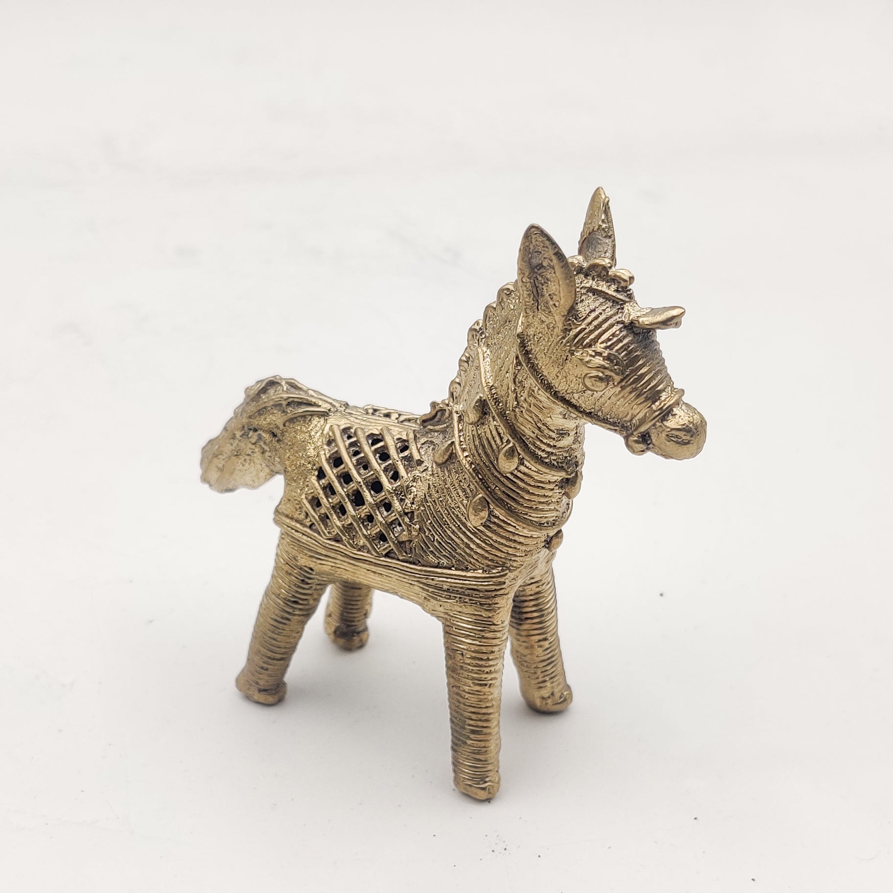 A gold-colored Dhokra horse figurine statue placed on a surface.