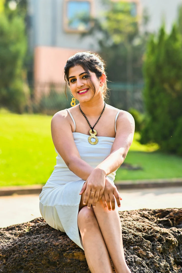 A woman sitting outdoors wearing a white dress and the Lucky Eight Tribal Necklace along with matching earrings.