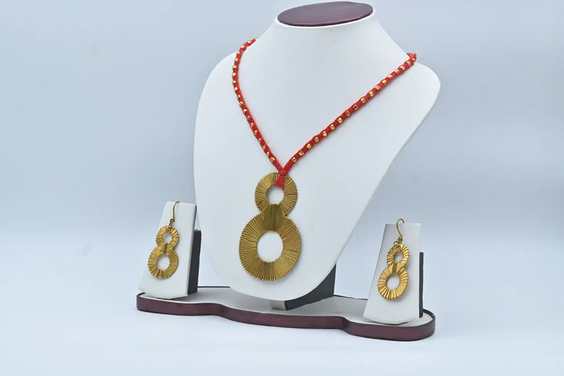 This jewelry set features a distinctive gold-toned "eight" shaped pendant and matching earrings paired with a red beaded necklace.