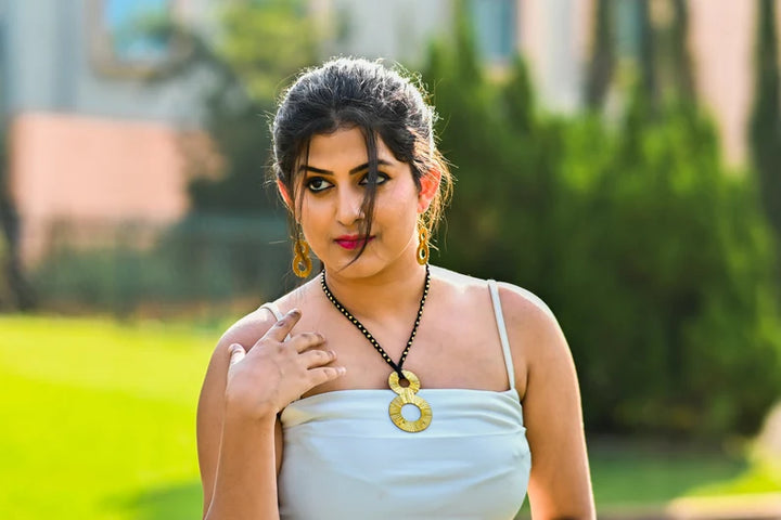 This image shows a woman wearing a light-colored, strappy top complemented by a distinctive pendant necklace and matching earrings.