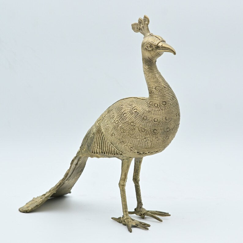 This item is a handmade metal peacock statue, likely crafted from brass using the traditional Dhokra art form. 